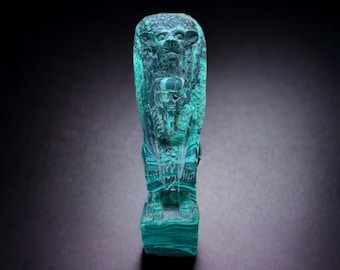 May include: A green stone sculpture of an Egyptian deity with a human head and a lion's body. The sculpture is carved in detail and has a smooth, polished finish.