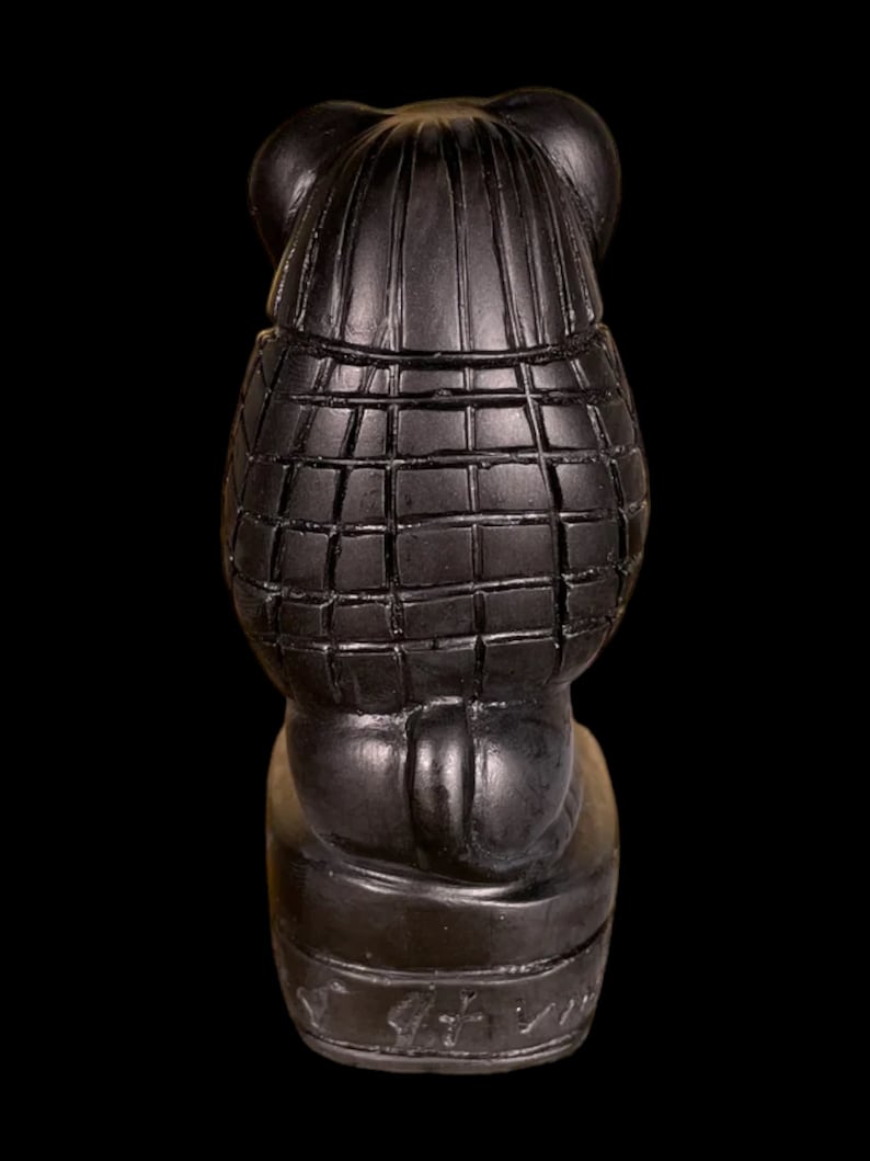 May include: Black ceramic figurine of a bear wearing a plaid coat and hat. The bear is sitting on a base with the word "Griffin" inscribed on it.