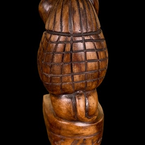 May include: A wooden carved figurine of a bear wearing a hat. The bear is sitting on a base with a carved inscription.