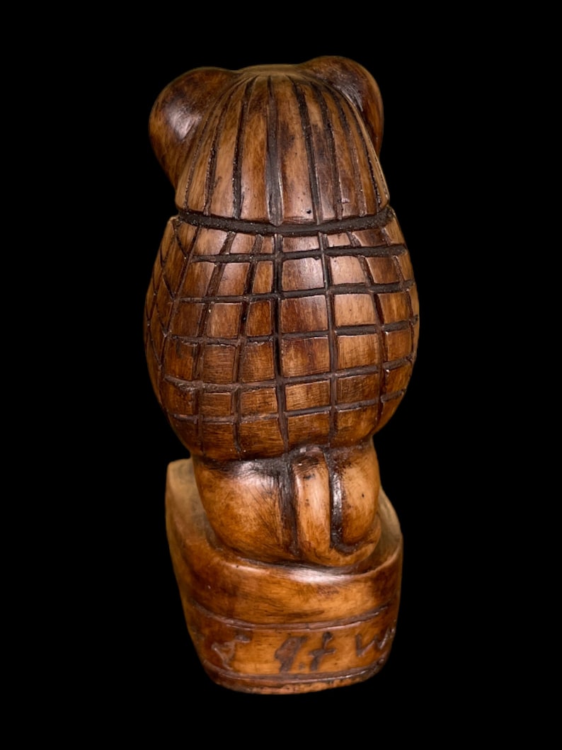May include: A wooden carved figurine of a bear wearing a hat. The bear is sitting on a base with a carved inscription.