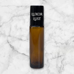 Op de afbeelding: Een bruine glazen rollerfles met een zwarte dop en een wit etiket met de tekst "LUXOR LUST".
