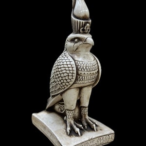 K&ouml;nnte beinhalten: Eine detaillierte, cremefarbene Statue einer falkenk&ouml;pfigen Gottheit, m&ouml;glicherweise Horus, mit aufwendigen Schnitzereien. Die Figur steht auf einem rechteckigen Sockel mit Hieroglyphen, vor schwarzem Hintergrund. Die Statue hat eine hohe Krone und detaillierte Federmuster.