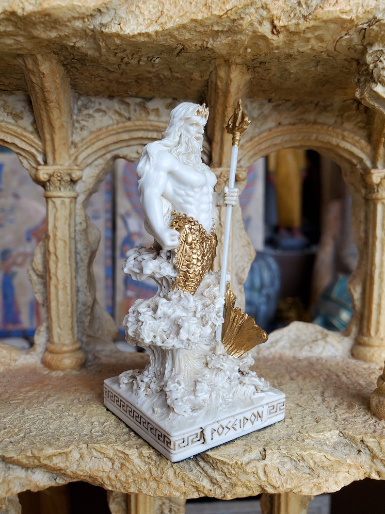 May include: White and gold statue of Poseidon, the Greek god of the sea, holding a trident. The statue is standing on a base with the word "POSEIDON" inscribed on it.