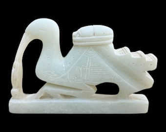 May include: A white jade carving of a bird with a long neck and a small, round object on its back. The bird is standing on a base.