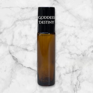 Op de afbeelding: Een bruine glazen rollerfles met een zwarte dop en een wit etiket met de tekst "GODDESS DESTINY".