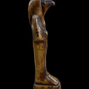 May include: A carved ivory statue of an Egyptian god with a falcon head. The statue is standing on a rectangular base.
