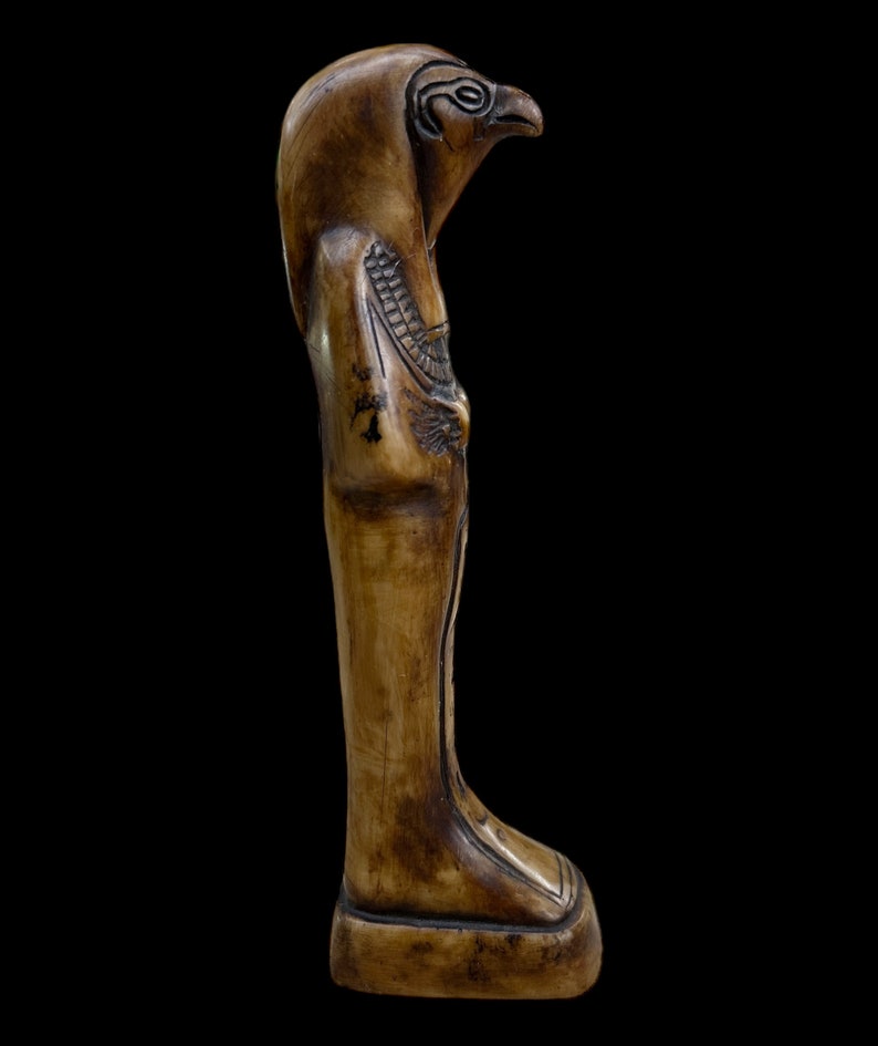 May include: A carved ivory statue of an Egyptian god with a falcon head. The statue is standing on a rectangular base.