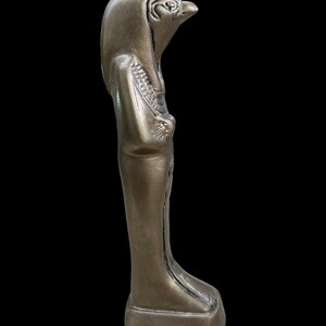 May include: A gold-colored statue of an Egyptian god with a falcon head. The statue is standing on a rectangular base.