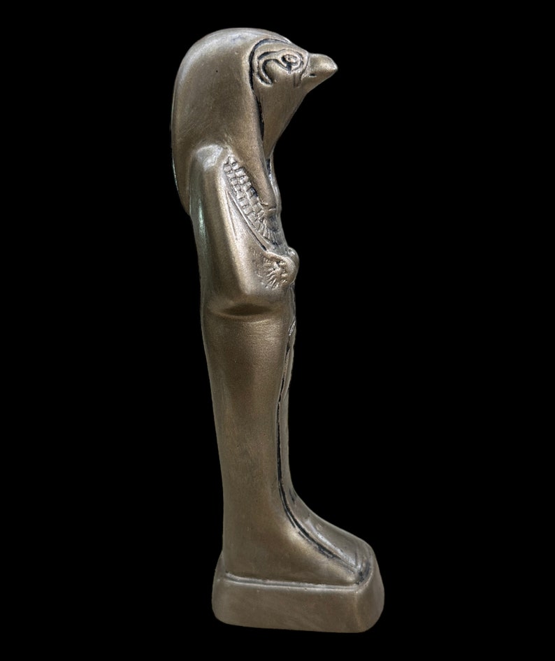 May include: A gold-colored statue of an Egyptian god with a falcon head. The statue is standing on a rectangular base.