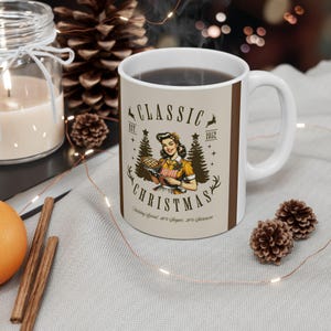 May include: White ceramic mug with a brown handle and rim, featuring a vintage-style illustration. The design includes the words "CLASSIC CHRISTMAS" and a retro image of a woman holding a pie. The mug has a light beige background.