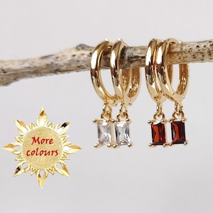 May include: Two pairs of gold hoop earrings with dangling rectangular stones. One pair has clear stones and the other pair has red stones.