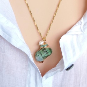 May include: A gold chain necklace with a green seashell pendant and a white pearl accent. The pendant is detailed with gold accents.