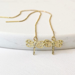 May include: A pair of gold-tone earrings with delicate dragonfly charms hanging from thin chains.