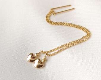 Può includere: Un paio di orecchini pendenti a forma di cuore in oro con una catena delicata. Gli orecchini sono sospesi da una sottile barra d'oro.