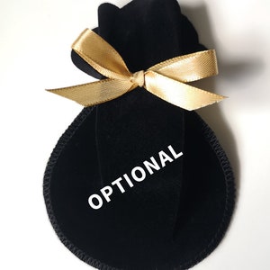 Pu&ograve; includere: Borsa in velluto nero con un nastro dorato legato a fiocco. La borsa ha la scritta "OPTIONAL" stampata.