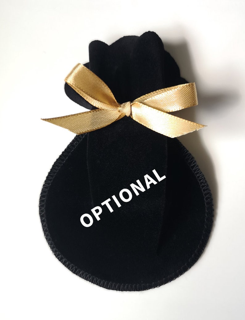 Pu&ograve; includere: Borsa in velluto nero con un nastro dorato legato a fiocco. La borsa ha la scritta "OPTIONAL" stampata.