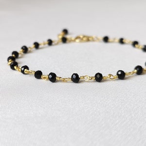 May include: A delicate gold chain bracelet with black beads. The bracelet is made with small, faceted black beads and a thin gold chain.