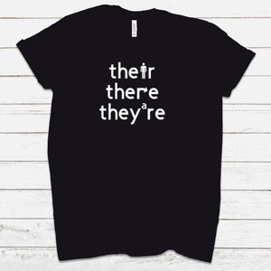 Puede incluir: Camiseta negra con texto blanco que dice "their there they're" con un figurín en lugar de la "a" en "they're".