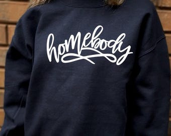 Puede incluir: Una sudadera negra con el texto "homebody" escrito en letras blancas cursivas.
