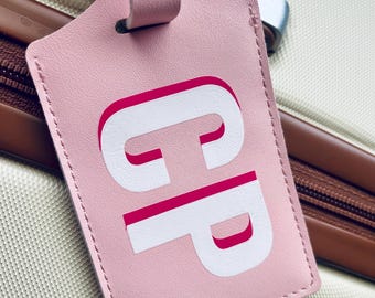 May include: Pink leather luggage tag with white letters "CP" in a bold, outlined font. The letters are outlined in pink.