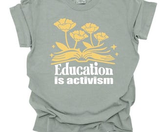 Könnte beinhalten: Hellgrünes T-Shirt mit gelbem Blumendesign über den weißen Worten "Education is activism". Das Design zeigt ein offenes Buch, Blumen und Sterne. Das T-Shirt hat kurze Ärmel und einen Rundhalsausschnitt.