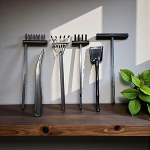 May include: A collection of dark metal gardening tools, including rakes, a trowel, and a curved tool, are displayed on a wooden shelf against a neutral wall. The tools have long, slender handles and are arranged in a row.