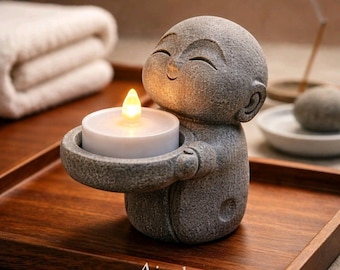 May include: A gray stone statue of a smiling Buddha holding a candle holder with a lit LED candle. The statue is on a wooden tray. The text "Airplantcrazy" is at the bottom of the tray.