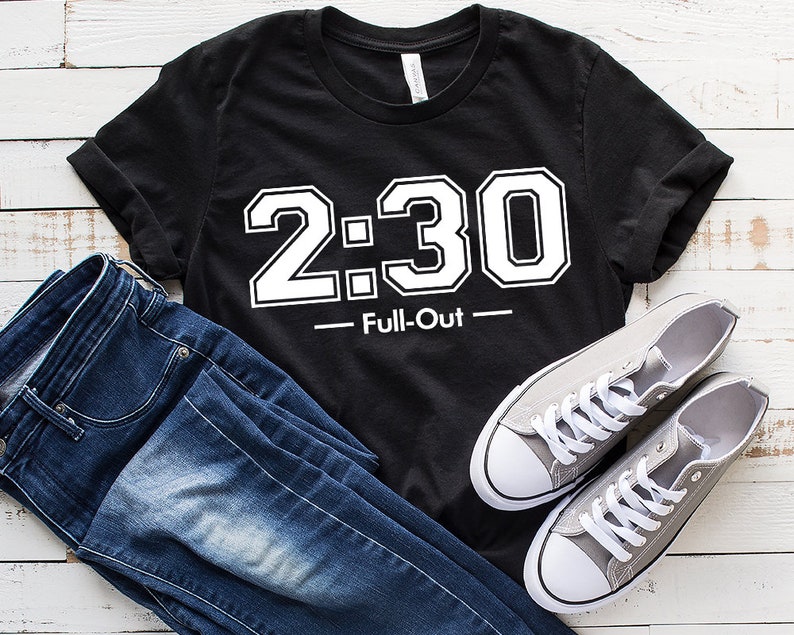 Peut inclure: T-shirt noir avec l'inscription blanche "2:30 - Full-Out". Le t-shirt est pr&eacute;sent&eacute; avec un jean bleu et des baskets grises en toile avec des lacets et des semelles blanches. L'ensemble est pos&eacute; sur une surface en bois blanc.