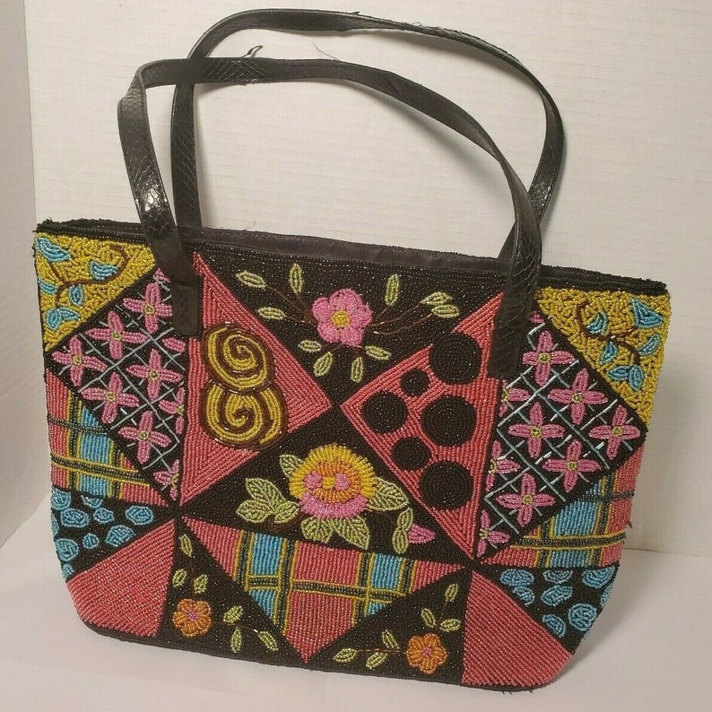 May include: A black tote bag with a patchwork design made of colorful beads. The bag has a black leather handle and a zipper closure.