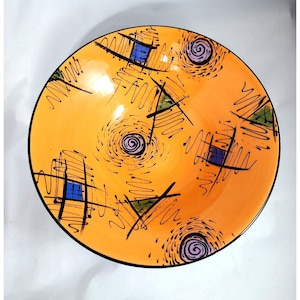 May include: Orange ceramic bowl with black, blue, and purple abstract designs. The bowl has a glossy finish and a black rim.