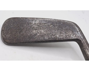 May include: A vintage golf club with a worn metal head. The club is marked "H.H. Gamble Special" and "AGS".