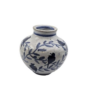 May include: A small, round ceramic vase with a speckled off-white glaze. The surface is decorated with hand-painted blue illustrations of birds perched on leafy branches. The rim features a solid blue band, and the interior is glazed in white.