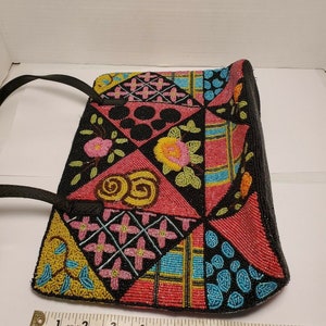 May include: A black beaded handbag with a patchwork design featuring various colors, including pink, blue, yellow, and green. The bag has a black leather strap and is decorated with floral and geometric patterns.