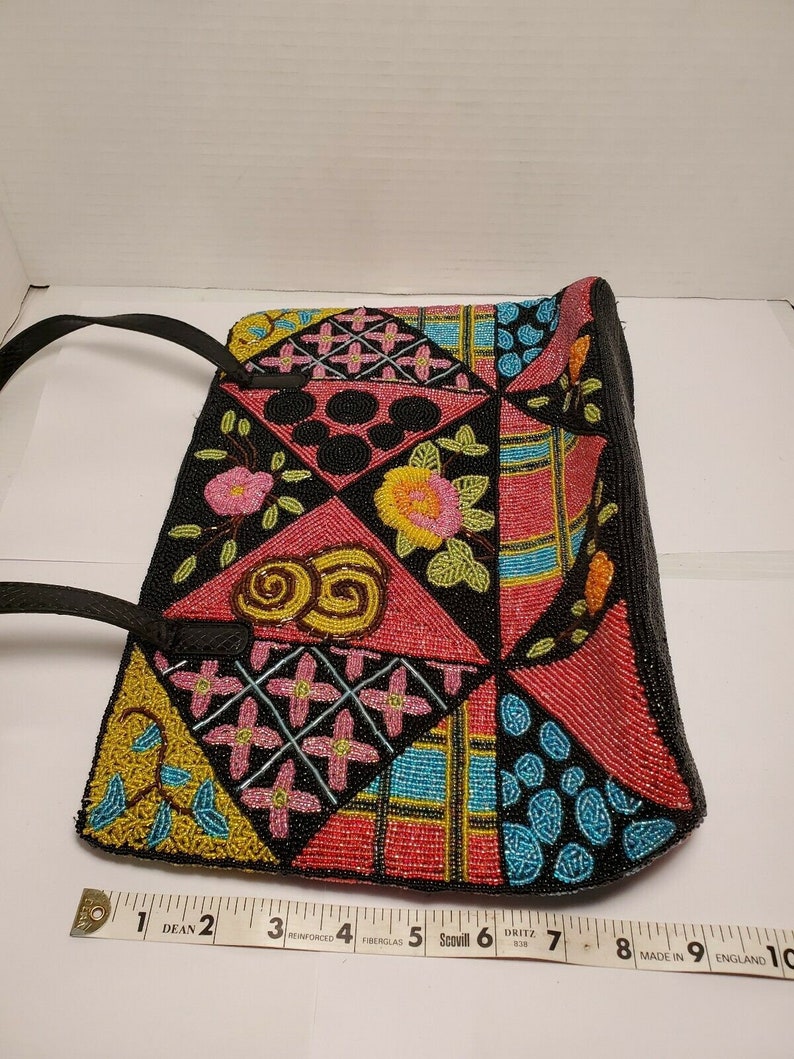 May include: A black beaded handbag with a patchwork design featuring various colors, including pink, blue, yellow, and green. The bag has a black leather strap and is decorated with floral and geometric patterns.