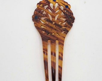 May include: A brown tortoiseshell hair comb with a decorative floral design and blue rhinestones.