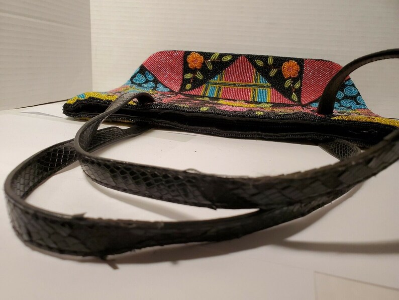 May include: A black beaded tote bag with a colorful geometric pattern and black leather straps. The bag has a zipper closure and is decorated with pink, yellow, blue, and green beads.