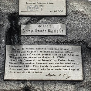 May include: A detailed, silver-toned metal buckle with text. The buckle is a limited edition, numbered 1097 of 10,000, from 1984. It features the Arroyo Grande Buckle Co. logo and historical text about Los Angeles.