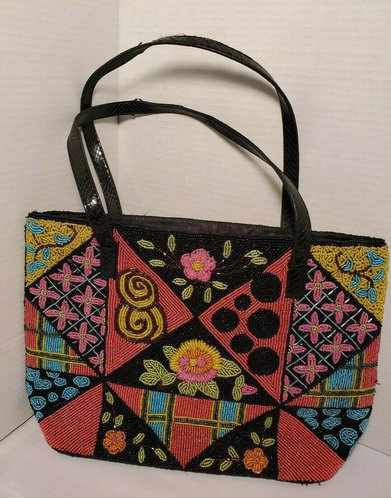 May include: A black tote bag with a patchwork design of colorful beads. The bag has black leather handles and a black lining. The beads are arranged in a geometric pattern with flowers and other designs.