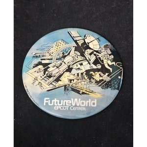 May include: A blue and white round button with a futuristic illustration of a city with a spaceship, a satellite dish, and an astronaut. The text "FutureWorld EPCOT Center" is printed on the button.
