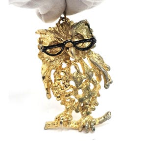 May include: Gold-tone owl charm with black glasses, perched on a branch. The owl has a detailed, textured design.