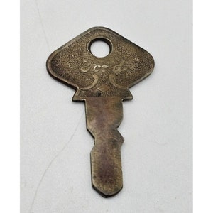 May include: A vintage brass key with a diamond-shaped head. The head is engraved with the word "Ford".