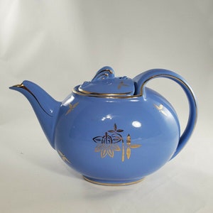 May include: A blue teapot with gold accents and a floral design. The teapot has a round body and a curved spout.