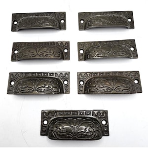 May include: Six antique bronze drawer pulls with ornate floral designs. The pulls are rectangular with a slight curve in the center.