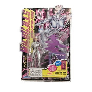 May include: A silver action figure of a female character in a metallic suit, packaged on a card with the text "WildC.A.T.S." and "Void". The packaging features a comic book style illustration and the text "Includes Special Edition Collector Card".