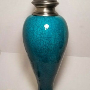 May include: A teal blue ceramic table lamp with a silver metal base and a crackled glaze finish.