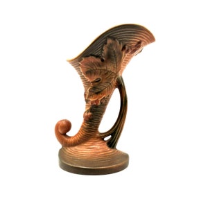 May include: A brown and green ceramic vase with a leaf design. The vase is shaped like a cornucopia and has a handle.