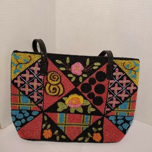 May include: A black tote bag with a patchwork design of colorful beads. The bag features geometric shapes and floral patterns in shades of pink, yellow, blue, and green.