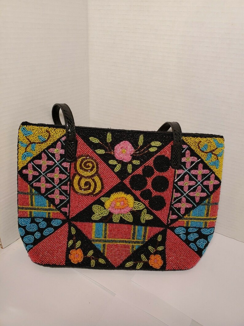 May include: A black tote bag with a patchwork design of colorful beads. The bag features geometric shapes and floral patterns in shades of pink, yellow, blue, and green.