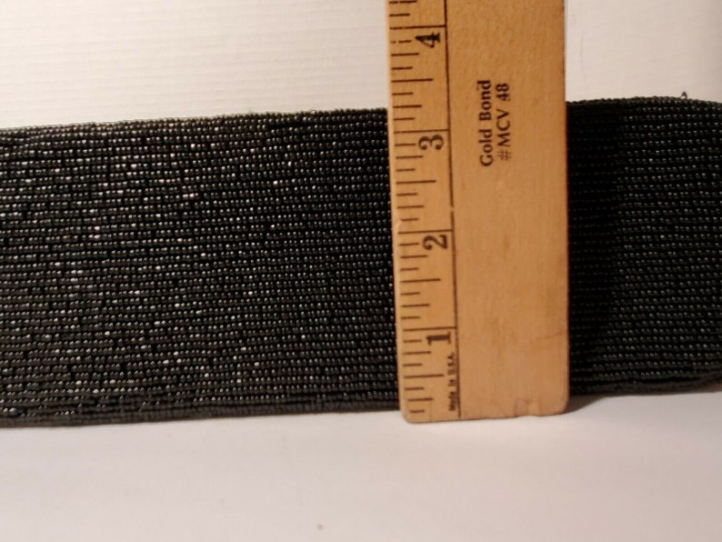 May include: A close-up of black beaded trim, measured with a ruler. The ruler shows measurements in inches and reads "Gold Bond #MCV 48".