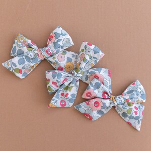 May include: Three floral print hair bows in shades of blue, pink, and green. The bows are tied with a knot in the center and have a vintage floral pattern.